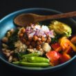 a blue bowl filled with vegetables and a wooden spoon