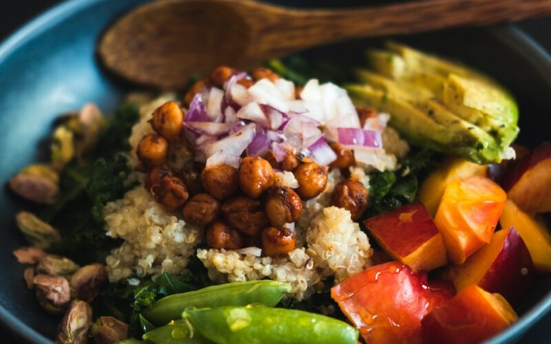 a blue bowl filled with vegetables and a wooden spoon