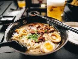 a bowl of ramen with chopsticks and a glass of beer