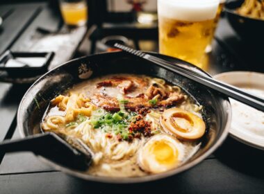 a bowl of ramen with chopsticks and a glass of beer