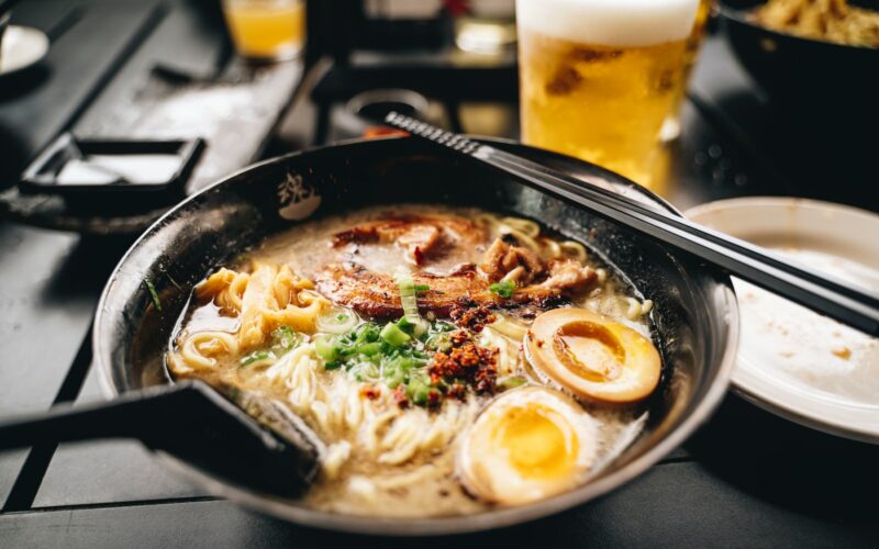 a bowl of ramen with chopsticks and a glass of beer