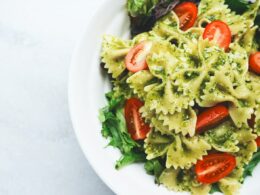 Pesto pasta with sliced tomatoes served on white ceramic plate