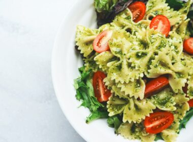 Pesto pasta with sliced tomatoes served on white ceramic plate