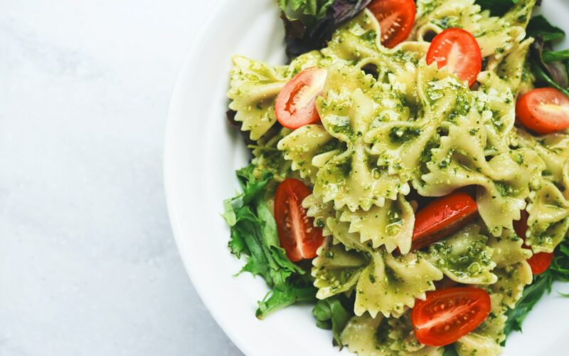 Pesto pasta with sliced tomatoes served on white ceramic plate